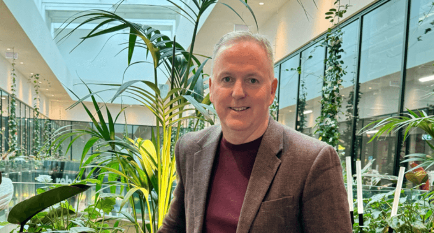 Man in a sports jacket stood in front of plants in a shopping centre